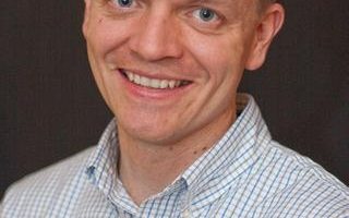an image of christopher oscarson smiling for a picture in a blue and white shirt