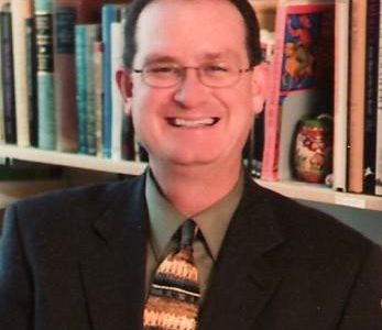 an image of a man in a suit and tie standing in front of a book shelf